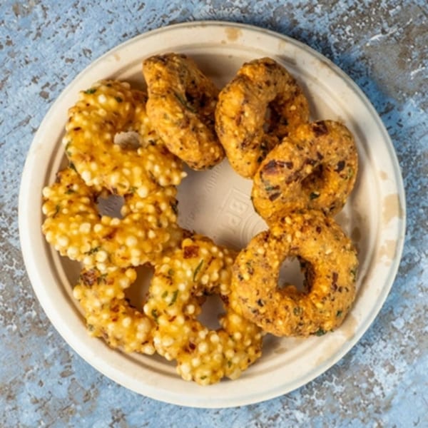 A plate of golden-brown, ring-shaped Indian vada and sabudana vada on a light blue surface.