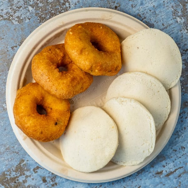 A plate of golden-brown vada and white idli, traditional Indian dishes, on a blue textured surface.