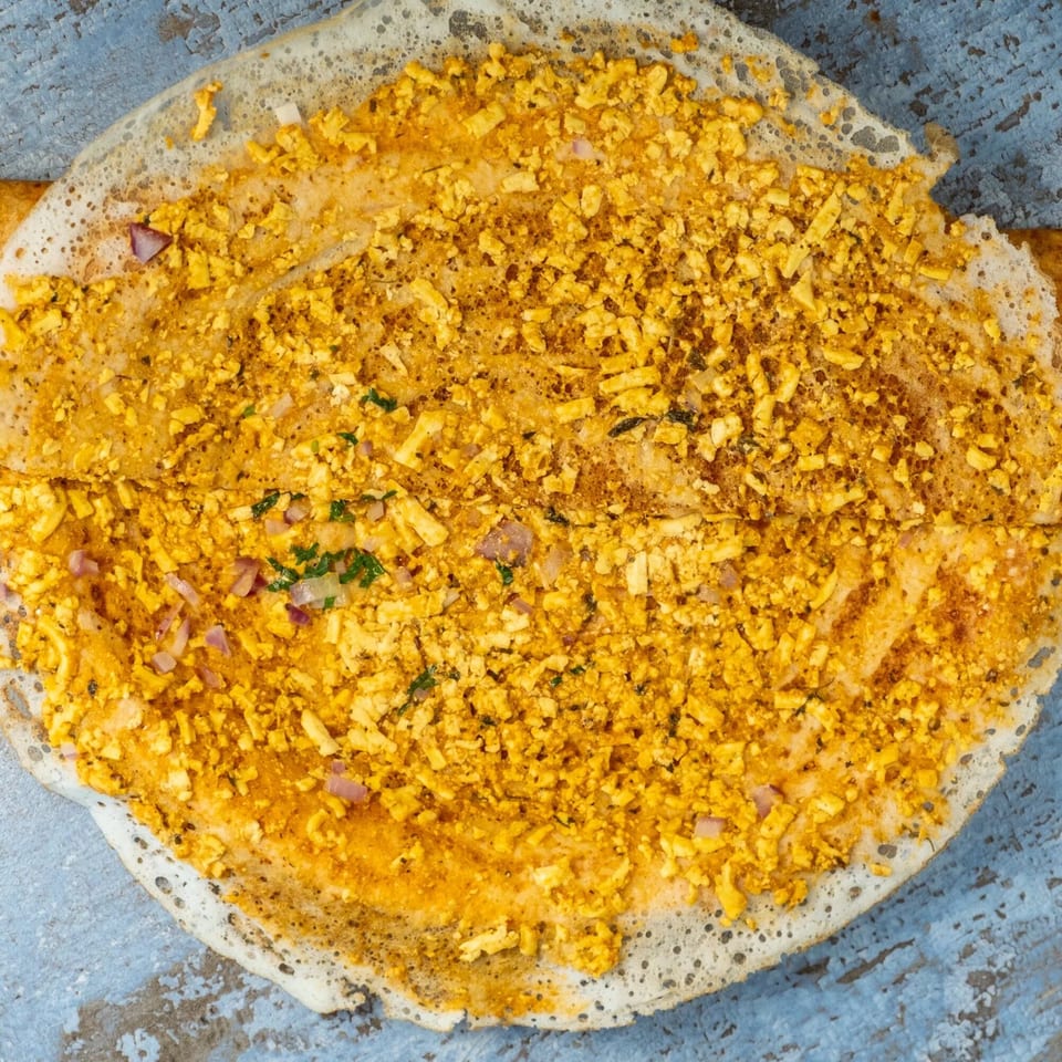 A close-up of a Hello! India paneer dosa, filled with crumbled paneer, onions, and herbs.