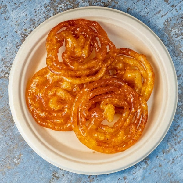 A plate of Hello! India's golden, syrupy jalebi, a traditional Indian sweet, on a blue background.