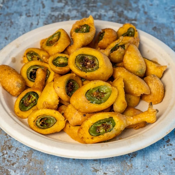 A white plate filled with golden-fried Indian chili pakora, showcasing green peppers within.