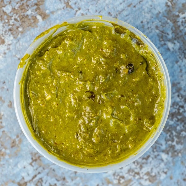 Overhead view of a clear plastic container filled with vibrant green Indian chutney.