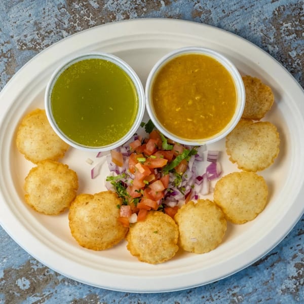 Pani Puri on a white plate with two dipping sauces and a side of chopped onions and tomatoes.
