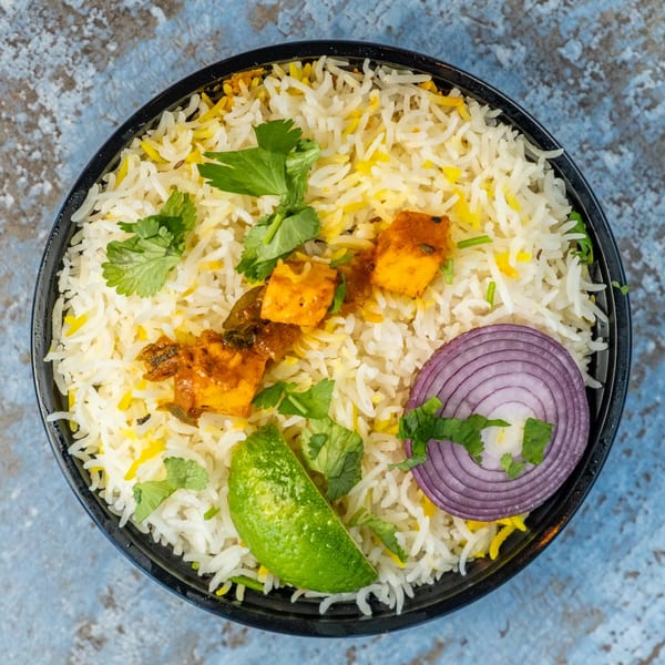 Hello! India's paneer biryani with rice, paneer, cilantro, red onion, and lime in a black bowl.
