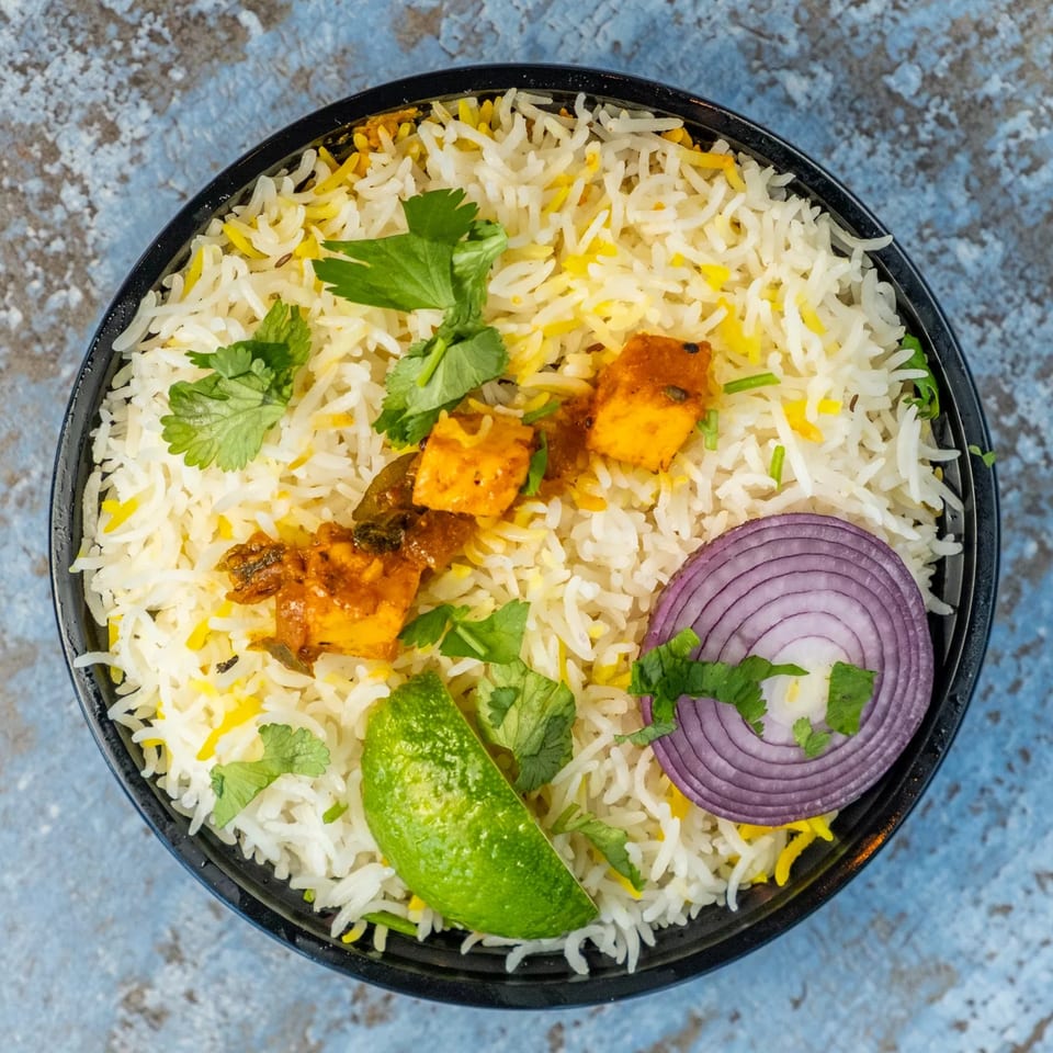 Hello! India's paneer biryani with rice, paneer, cilantro, red onion, and lime in a black bowl.