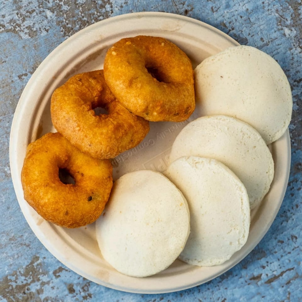 Hello! India's plate of three golden-brown vada and four white idli on a light plate.