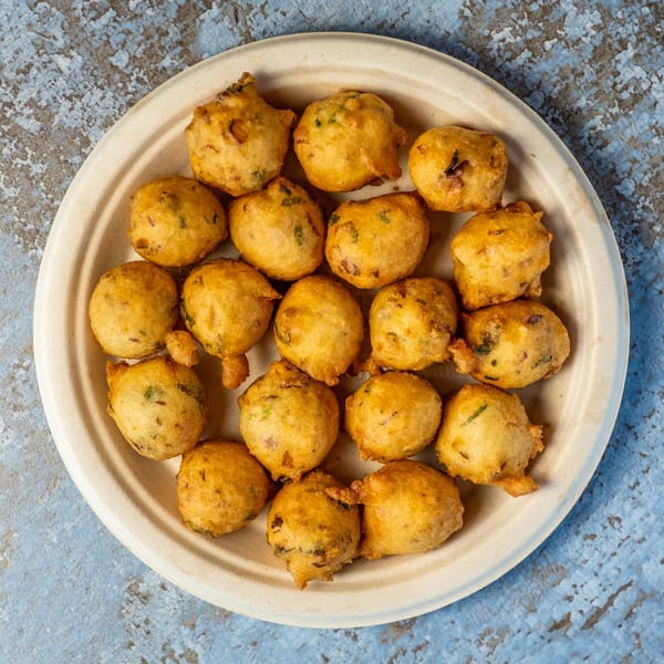 A plate of golden-brown, round Indian pakoras, a popular fried snack, on a light-colored plate.
