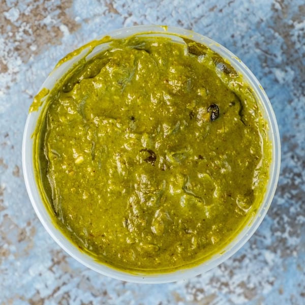 Overhead view of a white plastic container filled with vibrant green Indian chutney.