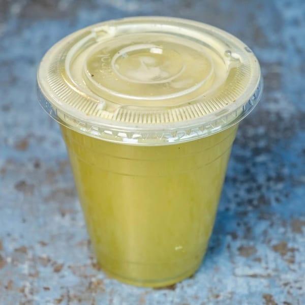 A clear plastic cup filled with a light yellow beverage, topped with a clear lid.