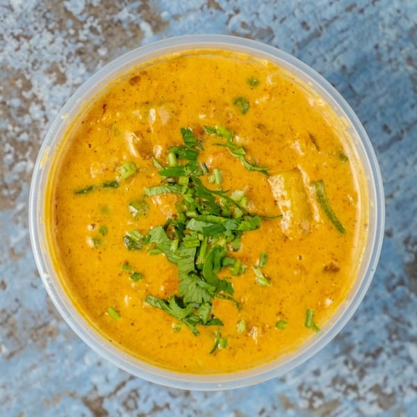 Overhead view of a vibrant orange Indian curry in a plastic container, garnished with fresh cilantro.