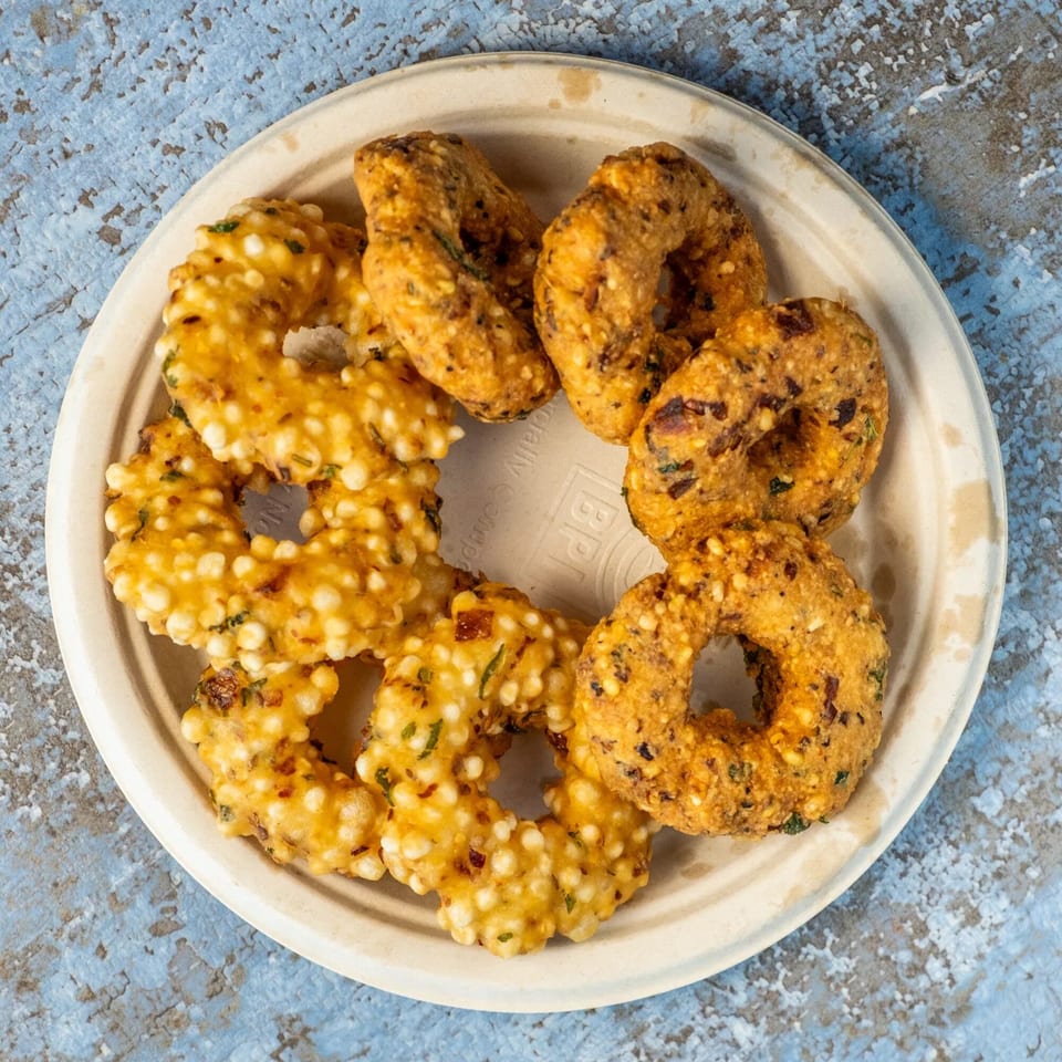 A plate of golden-brown, ring-shaped Indian fritters, some with visible white tapioca pearls.