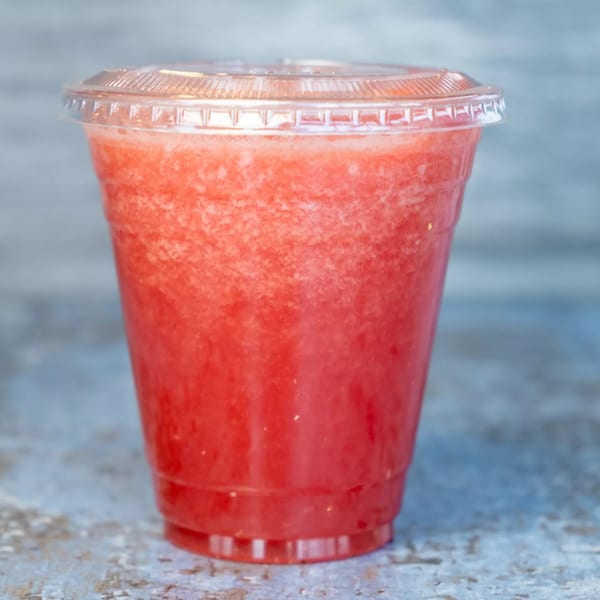 A vibrant red Hello! India strawberry smoothie in a clear plastic cup with a lid.